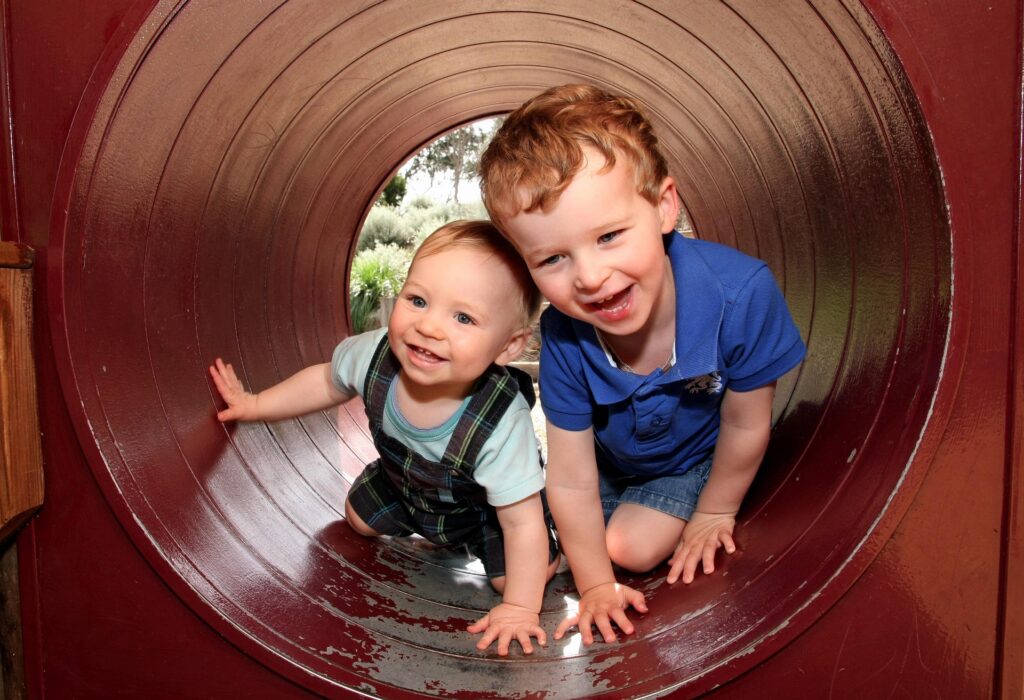 two children laughing while crawling through a tunnel while doing activities for 1 year old toddler