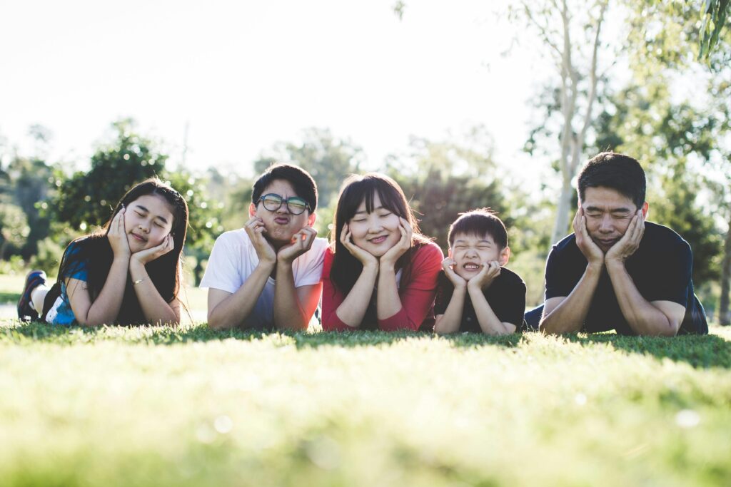 Asian family sitting happily on the grass in a sunny park while enjoying outdoor toddler activities and togetherness.