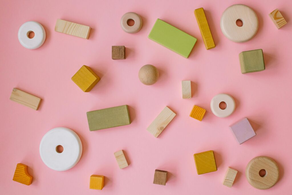 Flatlay of various wooden shapes on a pastel pink background to teach shapes to toddlers.