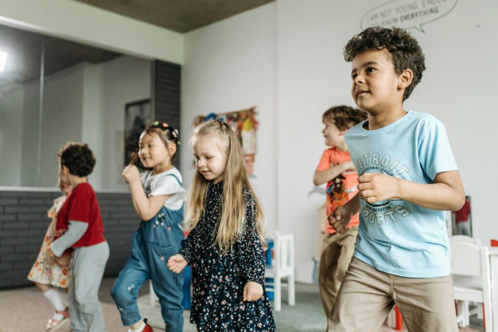 Energetic group of children dancing in a bright kindergarten classroom setting following the ultimate toddler activities.