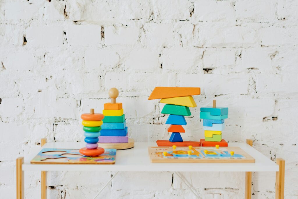 Vibrant wooden stacking toys displayed on a minimalist white table against a white brick wall.