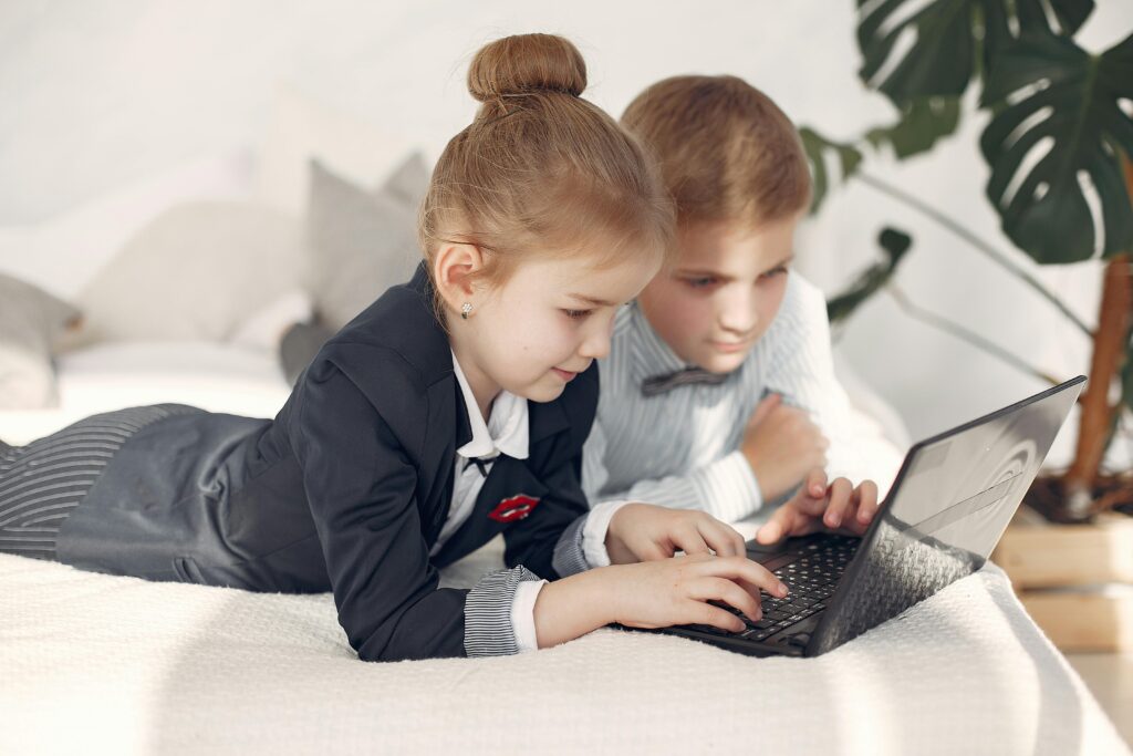 Two children dressed in formal attire using a laptop indoors, focused on learning.